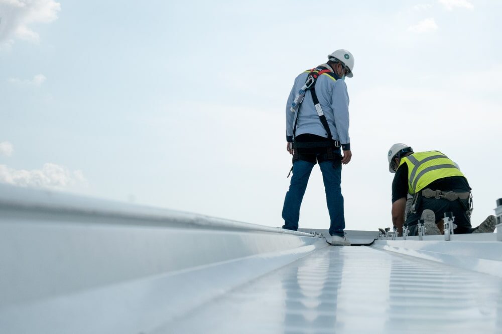 Man standing on a flat metal roof determining the cost to replace a commercial roof